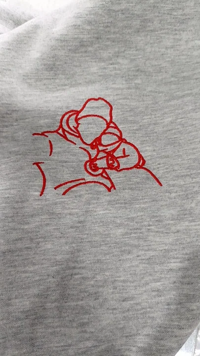 Kunde zeigt graues T-Shirt mit leuchtend roter Stickerei